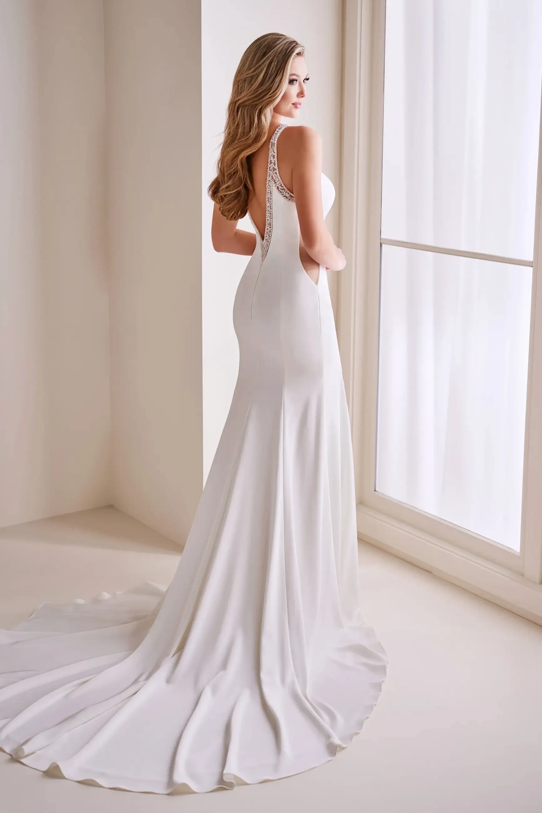 Model is wearing a stretch satin mermaid wedding dress with a jewel neckline, sleek cutouts, and intricate beading.