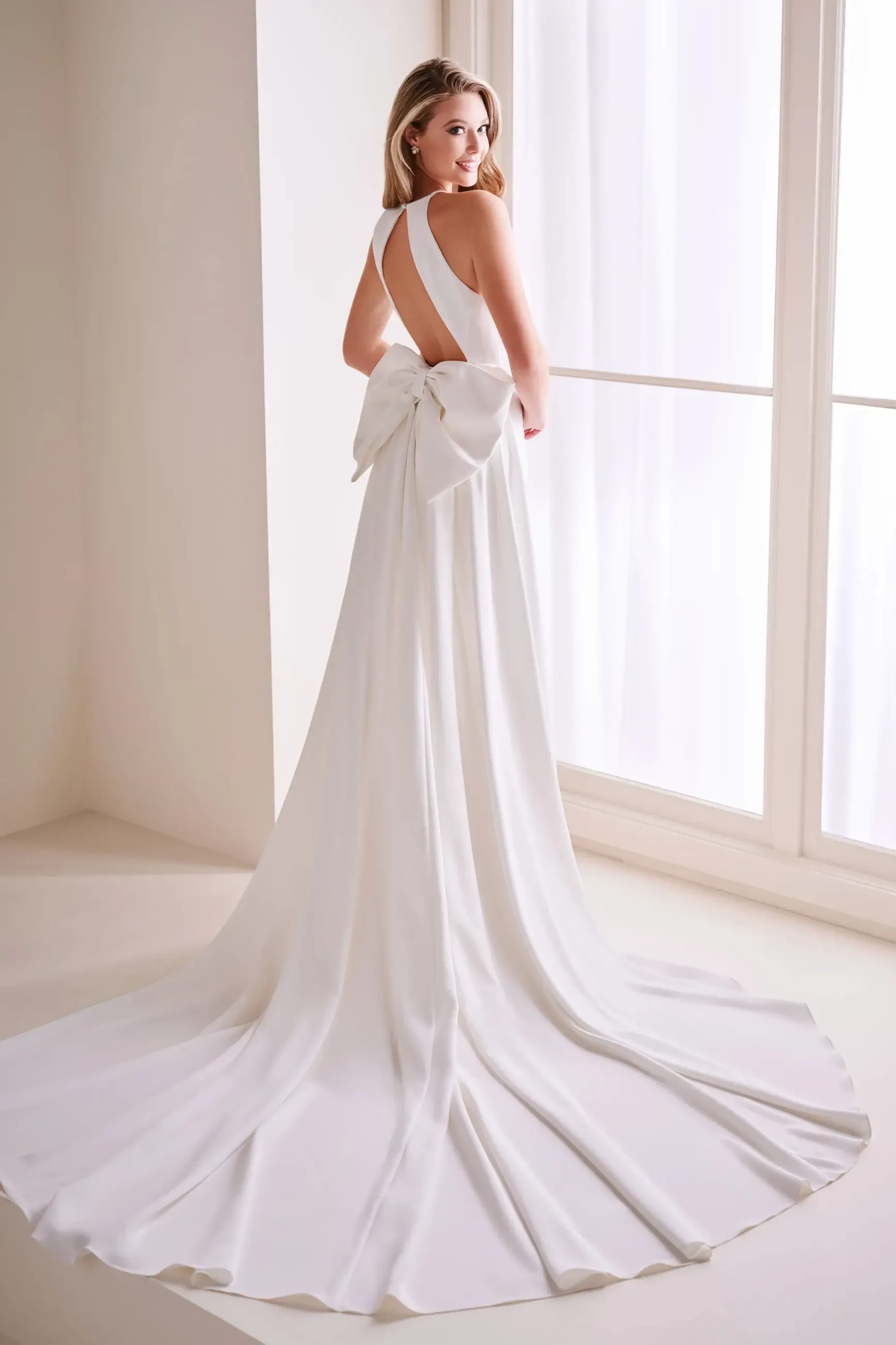 Model is wearing a sleek sheath gown with a high neckline, 3D flower accent, and a detachable 82-inch train.