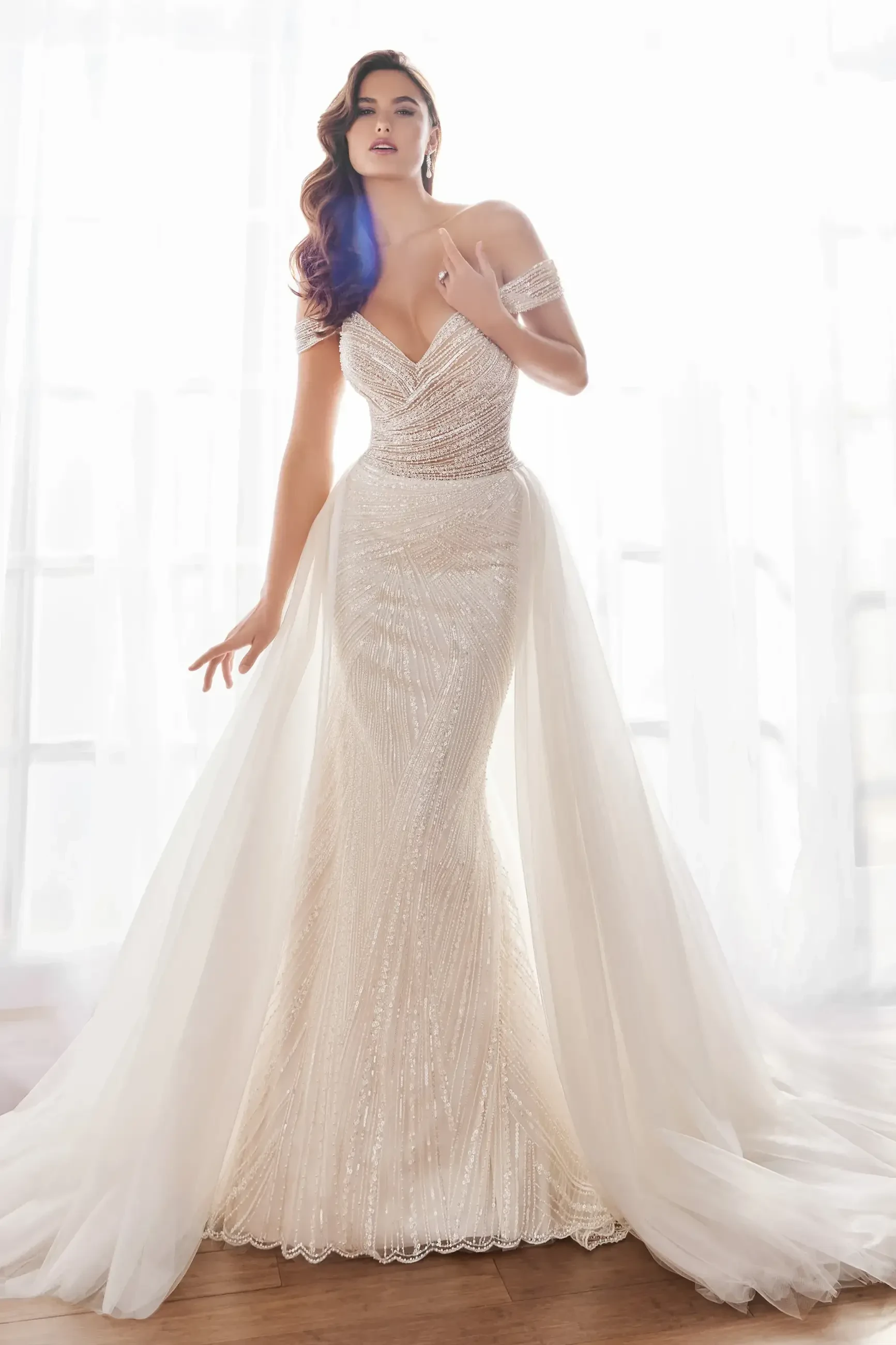 A woman wearing a beautiful, elegant wedding dress with intricate beadwork and flowing tulle, standing gracefully in soft lighting.