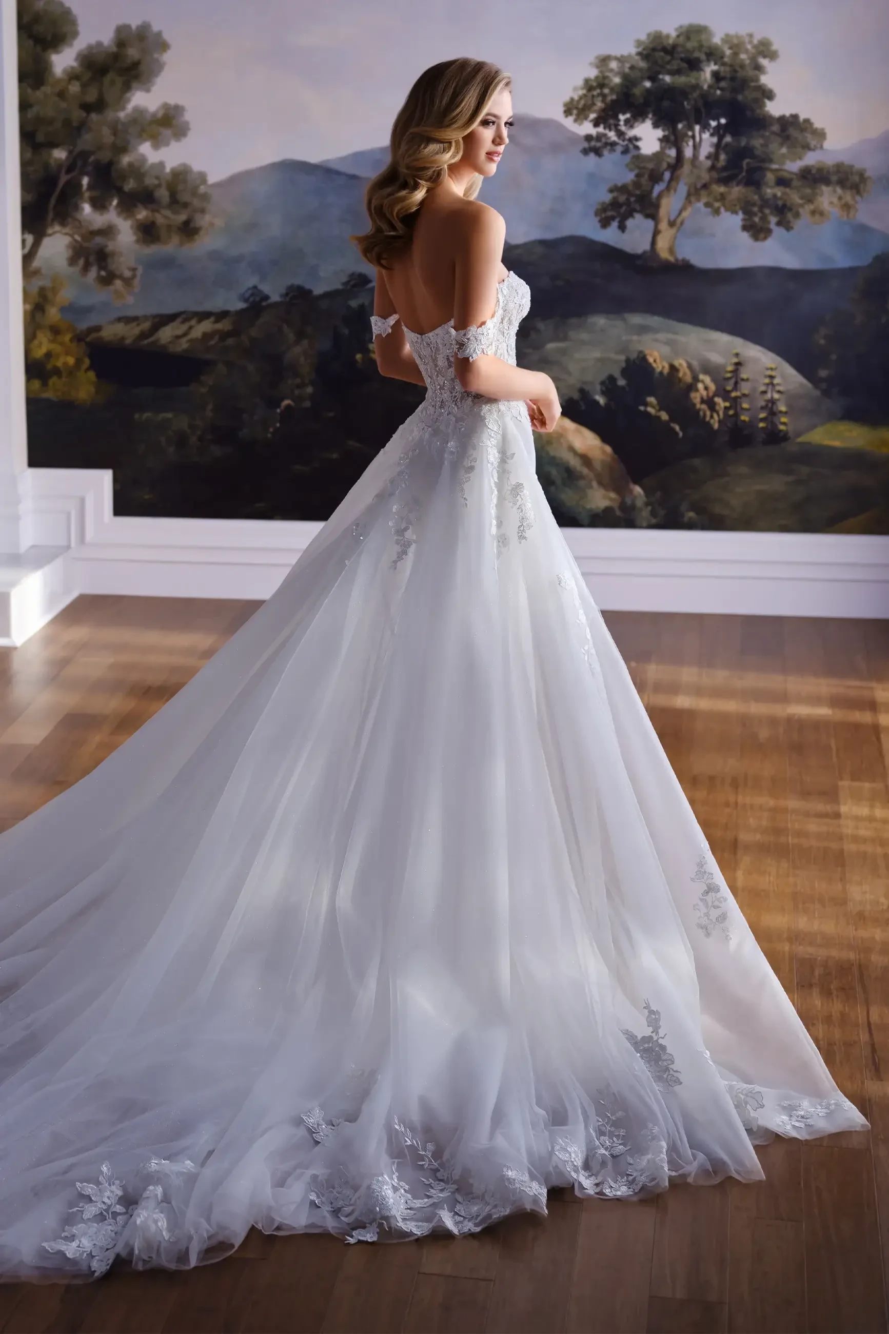 Model is wearing a crepe and lace mermaid gown with a plunging sweetheart neckline, semi-sheer bodice, removable off-the-shoulder straps, and a detachable train.